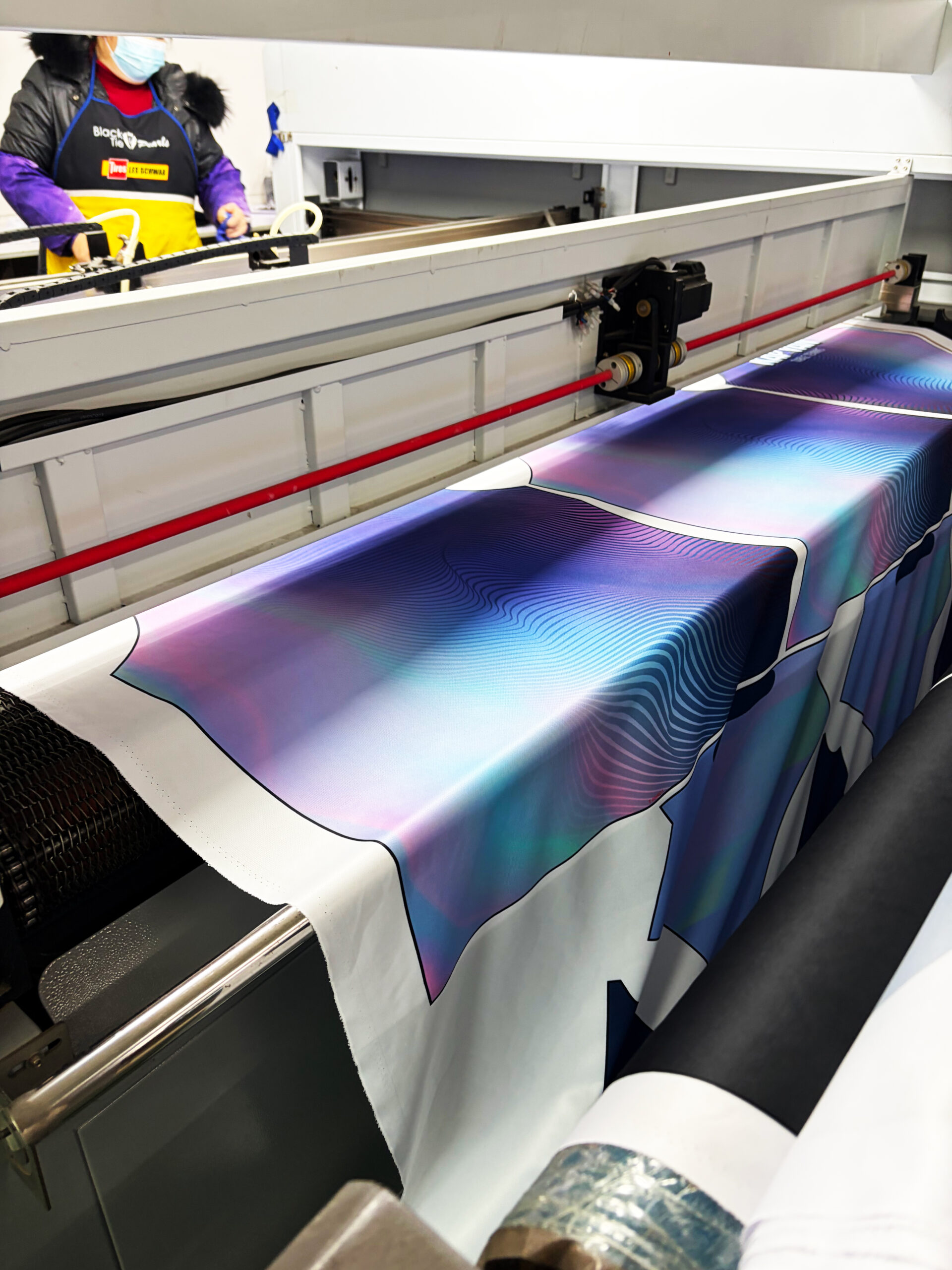 Operator loading polyester fabric roll onto industrial vacuum table of laser cutting machine
